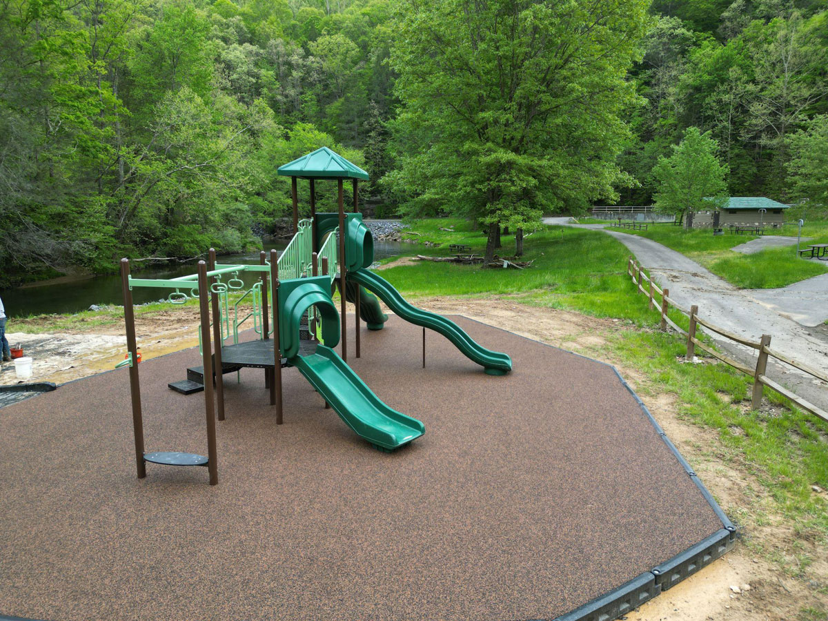 Green playground slides with rubber flooring in a wooded park setting