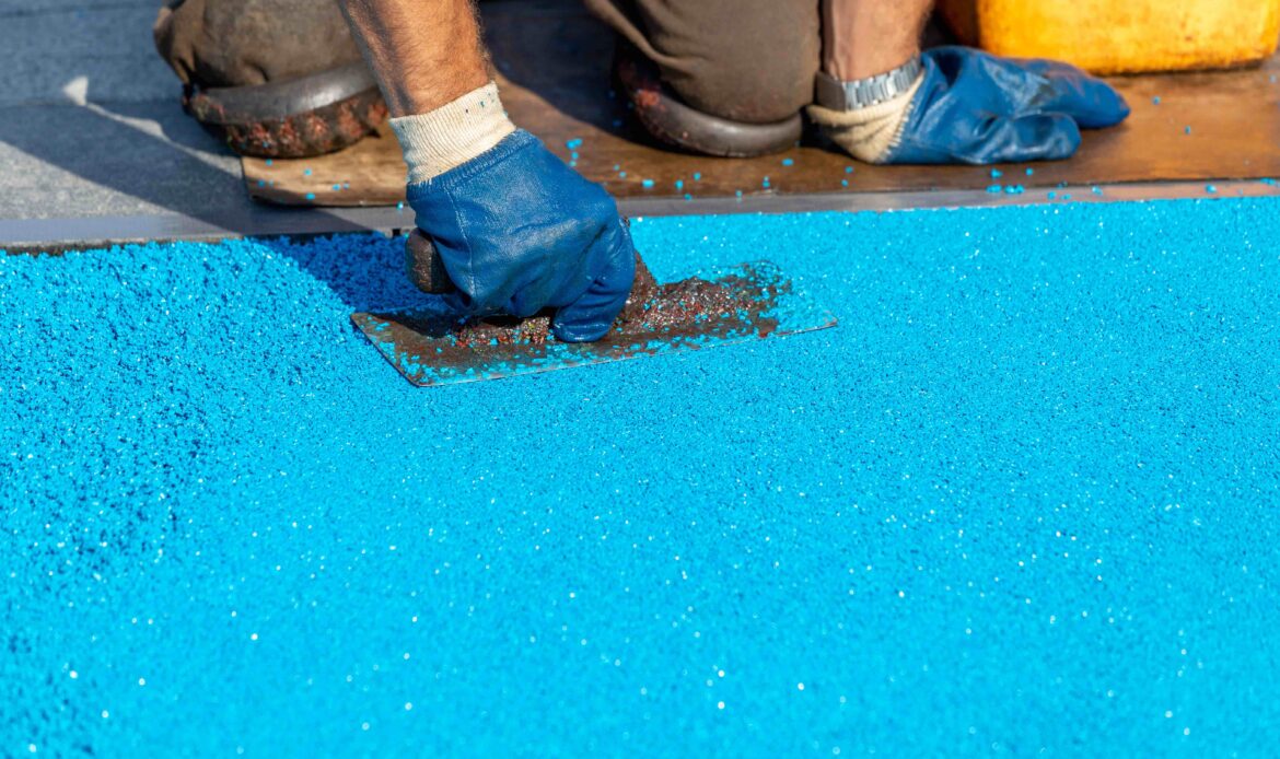 Worker applying blue rubber surfacing with a trowel for outdoor flooring installation