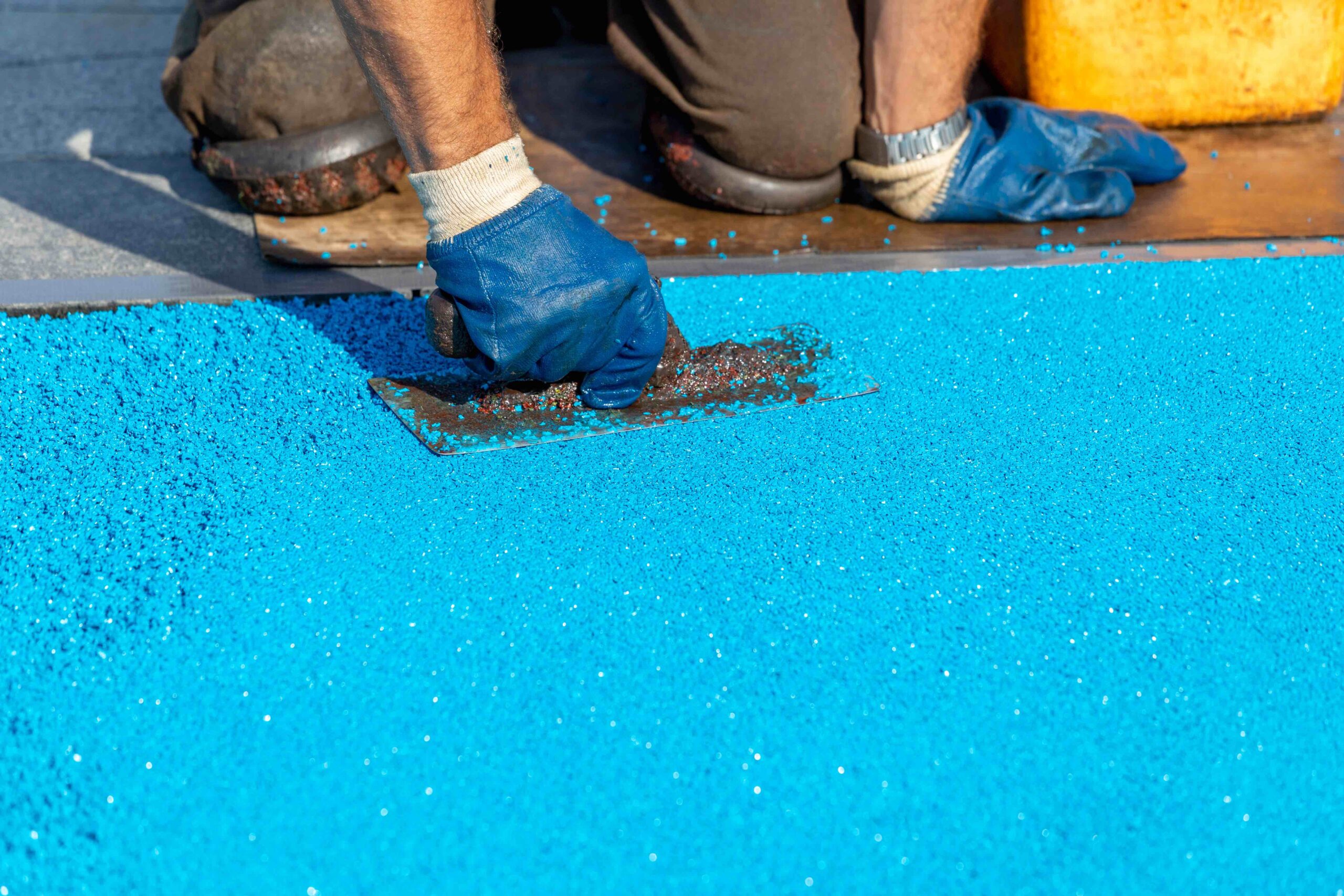 Worker applying blue rubber surfacing with a trowel for outdoor flooring installation