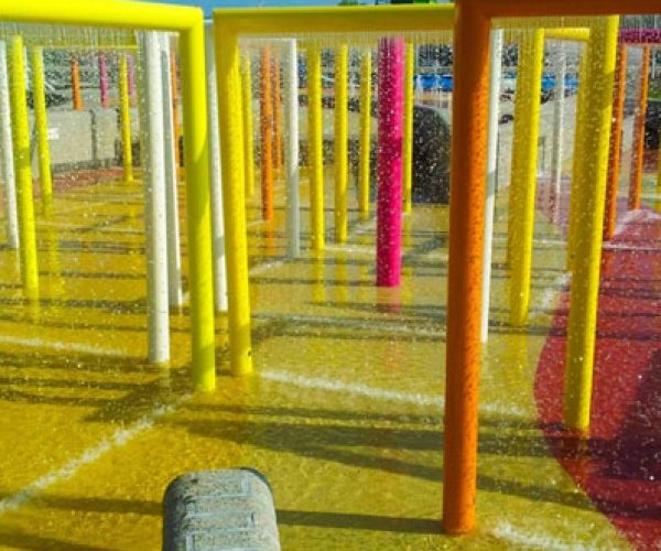Children enjoying a safe, slip-resistant kids’ play area with water shower, utilizing premium splash pad rubber surfacing. This innovative splash pad surface offers excellent cushioning to absorb impacts, reducing injury risk while maintaining durability and easy maintenance. Perfect splash pad surface options for Charlotte splash pads and splash pad surfacing across the United States.